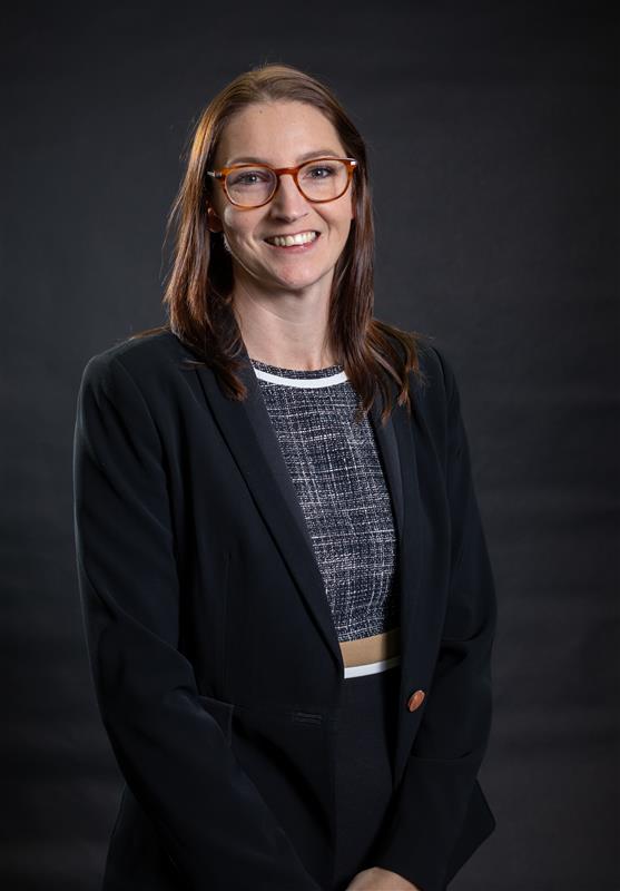 Portrait of Claire Owens, CEO of Alpine Group, smiling and wearing glasses and a dark blazer against a dark background